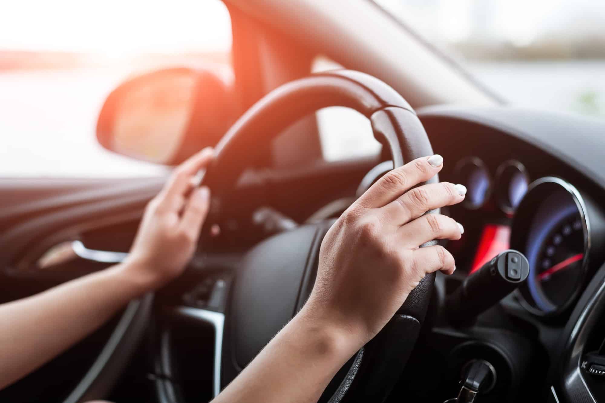 Women's hands on the steering wheel, inside the car.